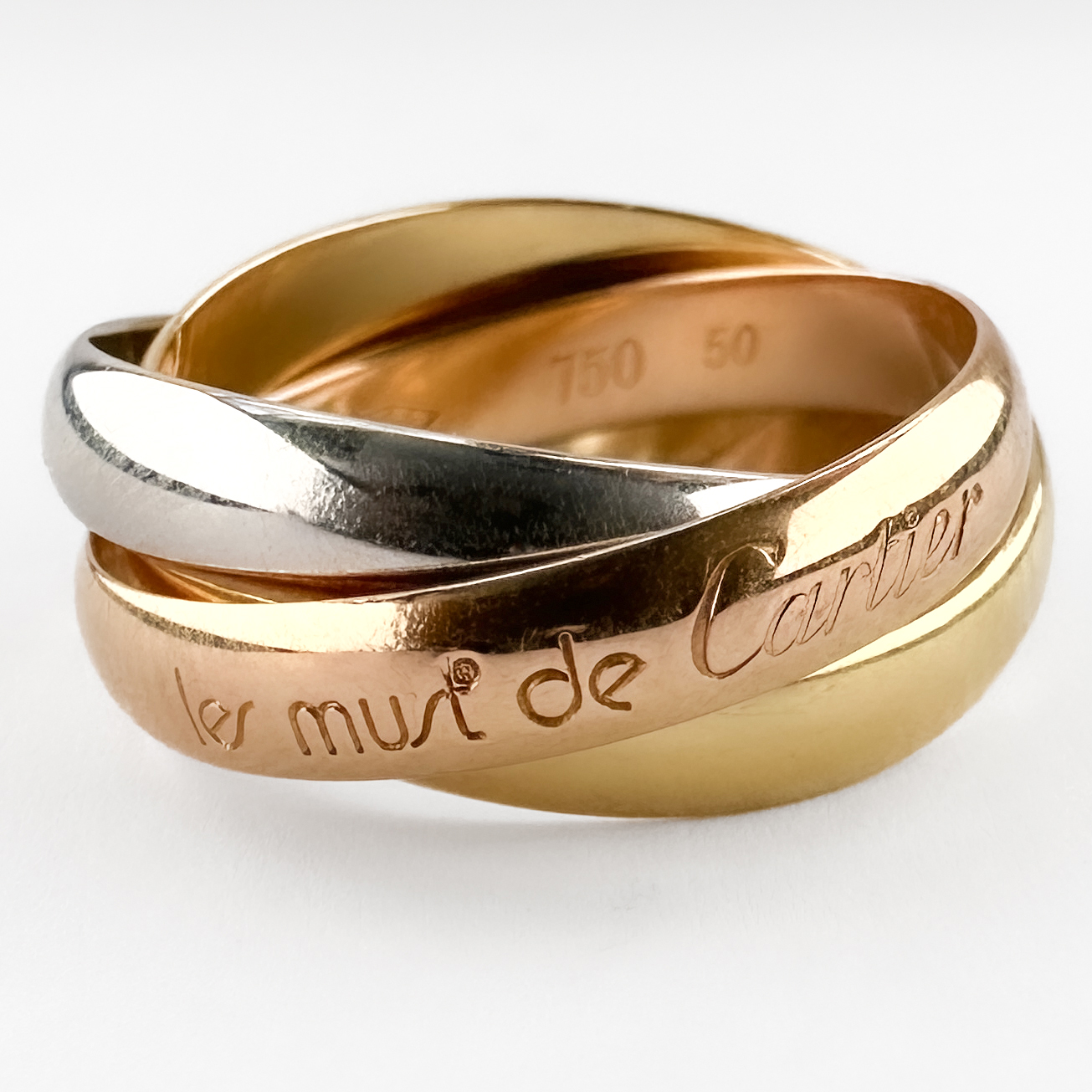 Les Must de Cartier Trinity Ring. This iconic Cartier design composed of three tricolour interlocking bands in 18ct yellow, white and rose gold. Originally created by Cartier in 1924, symbolises love, friendship and fidelity. The three bands move fluidly against one another, creating a timeless and effortlessly elegant piece. This example is marked “750” for 18ct gold, manufactured to the high standards associated with Cartier’s French production, the serial number is also stamped inside. The ring is also stamped with the Cartier signature and ring size '50'. A recognisable and enduring classic. This rings comes in its Cartier box. Please contact us if you would like to know more about this beautiful ring or visit us at Saddingtons Jewellery, Mayfair.