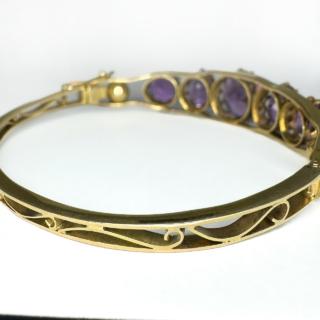 Antique Amethyst 5 Stone Gold Bangle.The top of this beautiful 5 graduating circular faceted amethysts,claw set within a galleried mount in polished yellow gold.The mounted amethysts are also set within 2 bands of gold with a gold sphere at each end.The bangle is hinged with a good strong hinge,there is a robust snap plate securing clasp with an additional figure of eight and ball securing clasp.The underside aspect of the bangle has graduating outer gold bands with ornate scrolling gold between the bands.A really beautiful bangle.The bangle is slightly oval allowing it to sit easily and comfortable on the wrist measuring 5.5 x 5.7 cm.Please contact us if you would like to know more about this bangle.