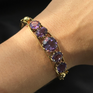Antique Amethyst 5 Stone Gold Bangle.The top of this beautiful 5 graduating circular faceted amethysts,claw set within a galleried mount in polished yellow gold.The mounted amethysts are also set within 2 bands of gold with a gold sphere at each end.The bangle is hinged with a good strong hinge,there is a robust snap plate securing clasp with an additional figure of eight and ball securing clasp.The underside aspect of the bangle has graduating outer gold bands with ornate scrolling gold between the bands.A really beautiful bangle.The bangle is slightly oval allowing it to sit easily and comfortable on the wrist measuring 5.5 x 5.7 cm.Please contact us if you would like to know more about this bangl
