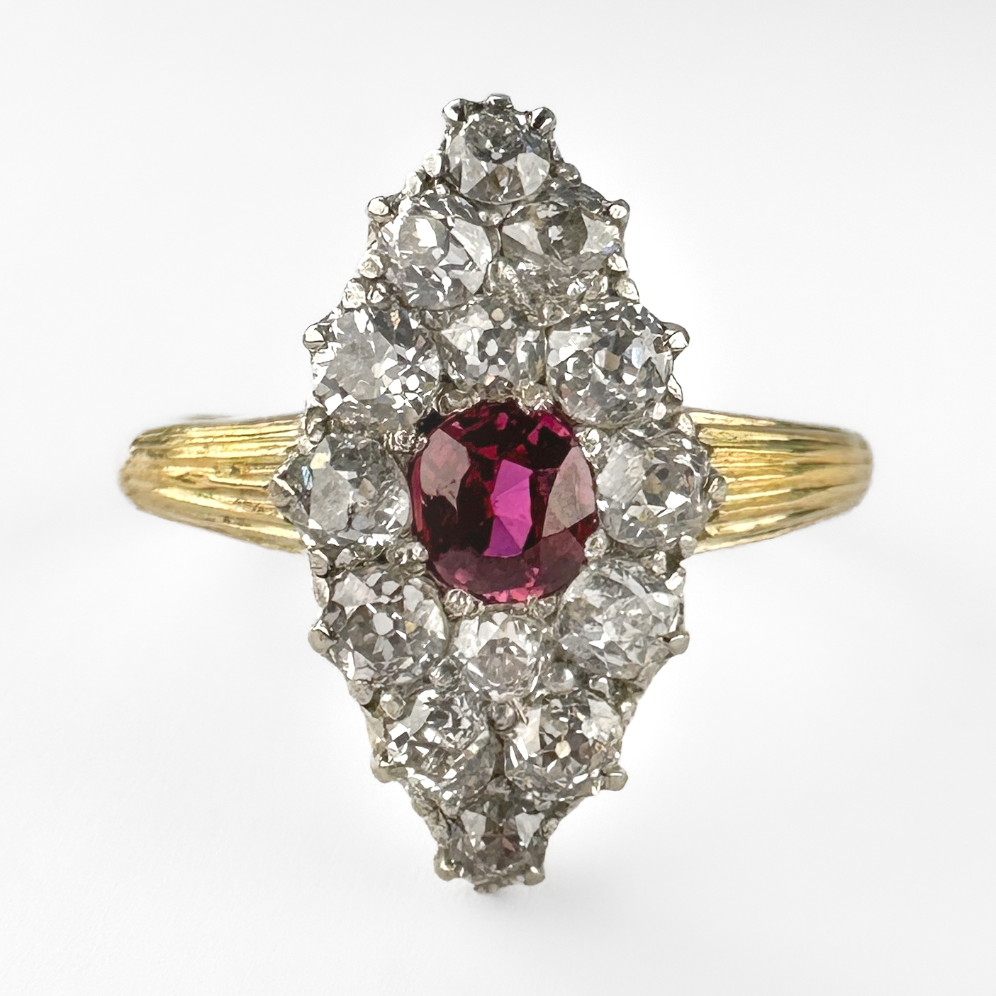 Elegant Diamond & Burma Ruby Marquise Ring. The ring features 14 twinkling old cut diamonds around a central red/pink old cut burma ruby. The shank is 18ct yellow gold with an 18ct mark. All the gems are claw set. The head of the ring measures at 1.8cm x 1cm and the ring sits low on the finger. This ring can be resized. Please contact us if you would like to know more about this stunning ring or visit us at Saddingtons Jewellery, Mayfair. 