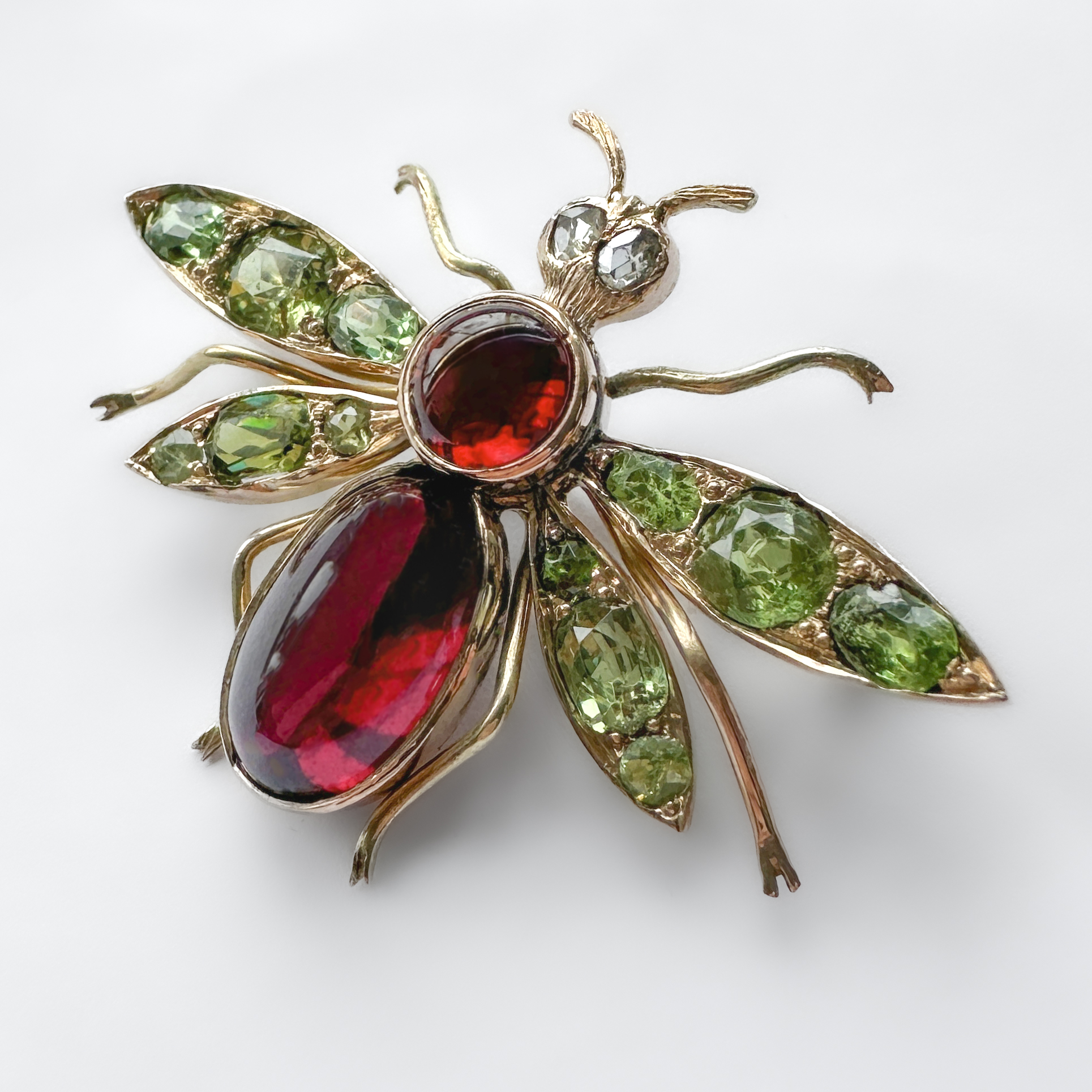 Antique Edwardian Bug Brooch. This sweet bug brooch features 12 vibrant green demantoid garnets on its 4 wings with 2 rich red garnets for its body and 2 diamonds for its eyes. All stones are set in 15ct yellow gold and measures at 1 inch x 1.45 inches. The bug also has a 15ct gold pin on the back. Please contact us if you would like to know more about this brooch or visit us at Saddingtons Jewellery, Mayfair.