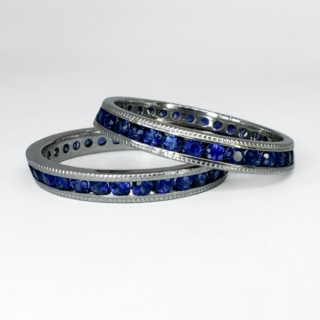 A Pair of Stacking Sapphire Eternity Rings. Both full eternity ring includes round cut royal blue sapphires that are channel set in 18ct white gold. The pair have a slight slope to their edges that make them perfect for stacking and other rings to sit between. They also feature millegrain detailed edging and are marked 1950s. The rings measure at  6mm in width when stacked on top of eachother. Please contact us if you would like to know more about these rings or visit us at Saddingtons Jewellery, Mayfair.