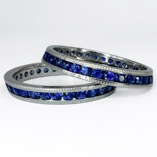 A Pair of Stacking Sapphire Eternity Rings. Both full eternity ring includes round cut royal blue sapphires that are channel set in 18ct white gold. The pair have a slight slope to their edges that make them perfect for stacking and other rings to sit between. They also feature millegrain detailed edging and are marked 1950s. The rings measure at  6mm in width when stacked on top of each other. As the rings are full sapphire ring bands, they cannot be resized. Please contact us if you would like to know more about these rings or visit us at Saddingtons Jewellery, Mayfair.