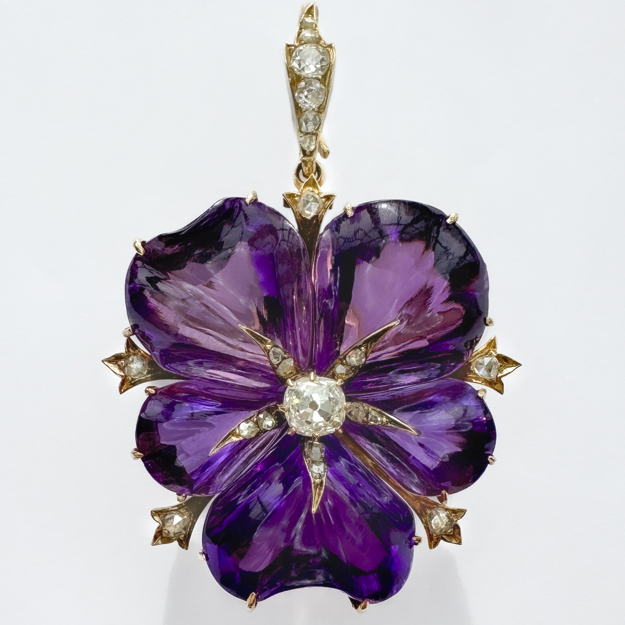 Stunning Late Victorian Amethyst & Diamond Flower Pendant. The flower has 5 beautifully carved vibrant purple amethyst petals in a 15ct yellow gold mount, the diamonds in the centre, on the outside and on the pendant fitting are also set in 15ct yellow gold. The piece measures at 1.4 x 3 inches and comes in its original box. At the back of the pendant, the fixings are also in 15ct yellow gold, these removable fixings will convert the pendant to a brooch. The chain is for display purposes only, chains are available on request. Please contact us if you would like to know more about this unique antique pendant/brooch or visit us at Saddingtons Jewellery, Mayfair.