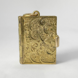 Intricate And Rare Antique Book Locket. The book is in 15ct yellow gold. It has remarkable hand carved scrolls and flowers to the book cover. There is a wide clasp to secure the opening of the book. On opening there are 4 oval hinged frames( 2 on each side), to hold memorabilia or photos. The condition of this locket is excellent. On the top of the book is a large bale to attach a chain with is not provided with this locket. The book measures 2.5 x 2 x o.5 cm. A Beautiful locket. Please contact us if you would like to know more about this locket or visit Saddingtons Jewellery, Mayfair.