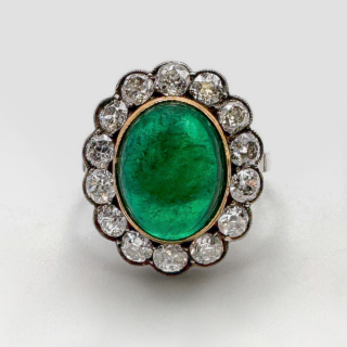 Rare and Beautiful Antique Large Cabochon Emerald Cluster Ring.This large columbian emerald ring is set in 18ct yellow gold and platinum shank.The central 7.65ct cabochon emerald is surrounded by 14 antique diamonds set in platinum and is graine set.Please contact us if you would like to know more about this ring.