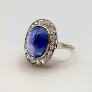 5.5ct Art Deco Burma Sapphire Cabochon Diamond Ring.Exquisite Burma sapphire cabochon diamond cluster ring.The central sapphire is certificated no heat.Surrounded by bright antique diamonds, set in platinum and all gems are graine set.This stunning ring is comfortable to wear and sits low on the finger.Please contact us if you would like to know more about this stunning ring.