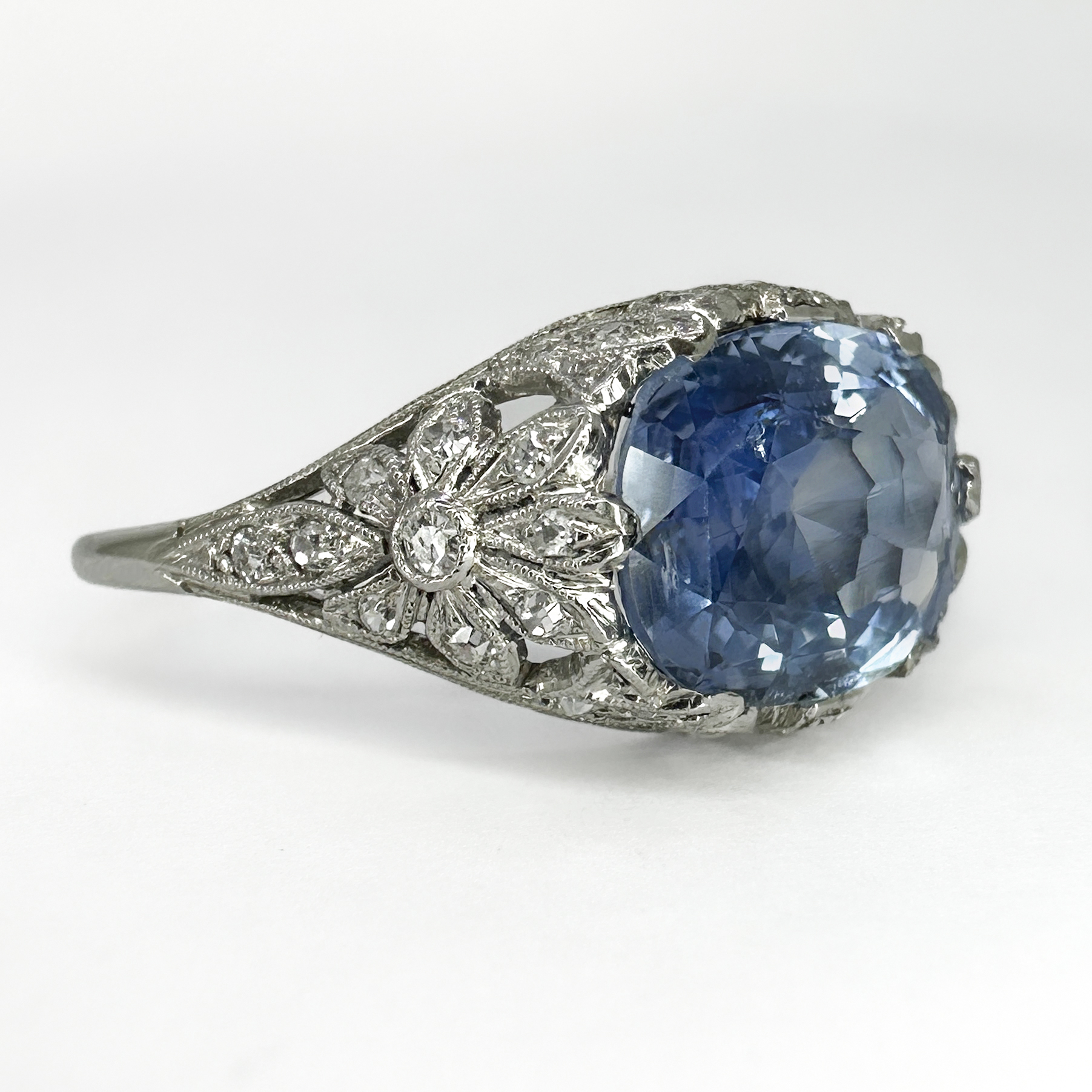 Exquisite and Stunning Antique 4ct Sapphire And Diamond Ring. The long oval natural no heat Ceylon light blue sapphire which is cushion cut measures 1.2 x 0.8 cm on the head of the ring. The sapphire is set with claws are finely stylised flowers and scrolls which have small old cut diamonds graine set through out the shank and shoulders of this beautiful ring. The shank is platinum. This unusual and beautiful ring sits comfortable on the finger. It can be resized, please contact us or visit us at Saddingtons Jewellery, Mayfair if you would like to know more about this ring.