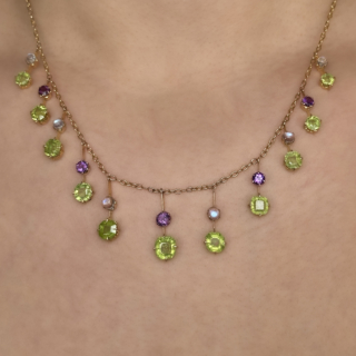 Arts and Crafts Suffragette Fringe Necklace. This stunning necklace features 11 drop peridots with moonstones and amethysts alternating. The necklace is made from 18ct yellow gold and the stones in the necklace are claw set. The necklace measures at 18 inches and has a drop of 1 inch. Please contact us if you would like to know more about this ring or visit us at Saddingtons Jewellery, Mayfair. 